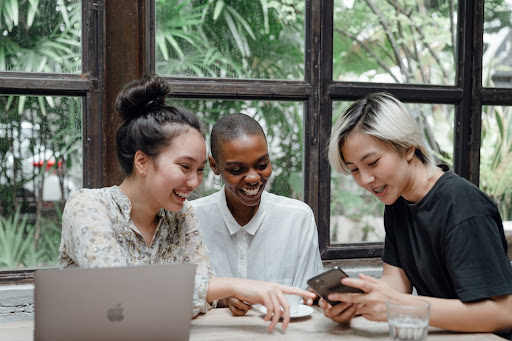 Three women engaged in lively conversation over cups of coffee while sitting in front of a computer.