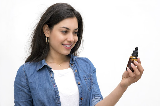 A girl with a bright smile, holding bottles of CBD oil in her hands. Her expression exudes a sense of contentment and well-being, highlighting the positive impact and enjoyment that CBD products can bring to one's life.
